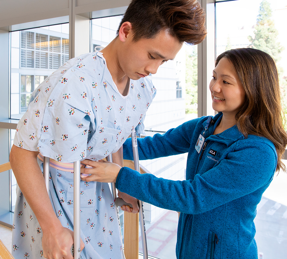 Female physical therapist helping male patient on crutches