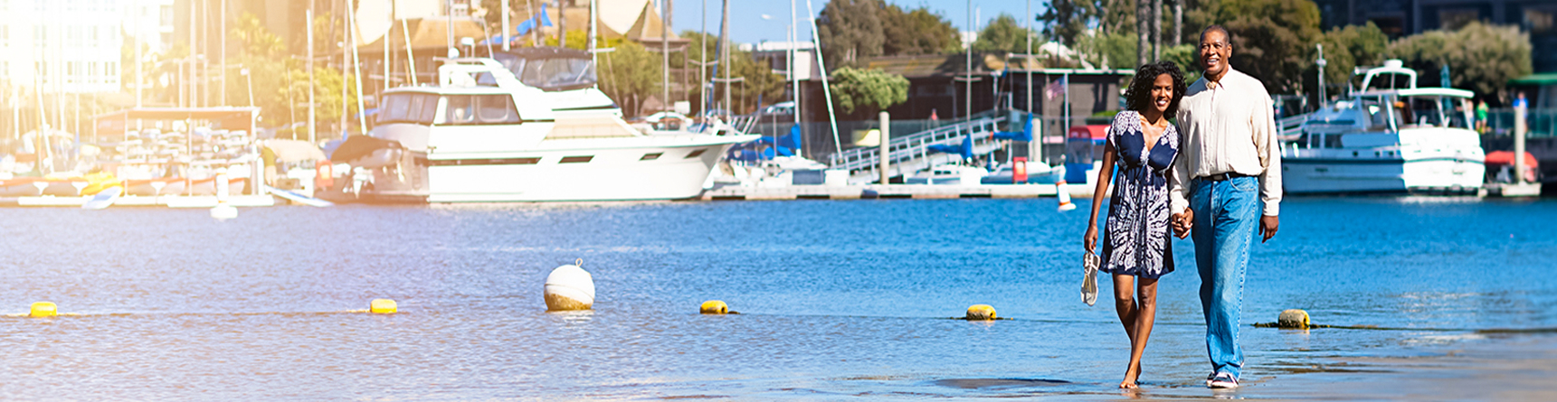 Couple walking on shore with docks, yachts and sailboats in background