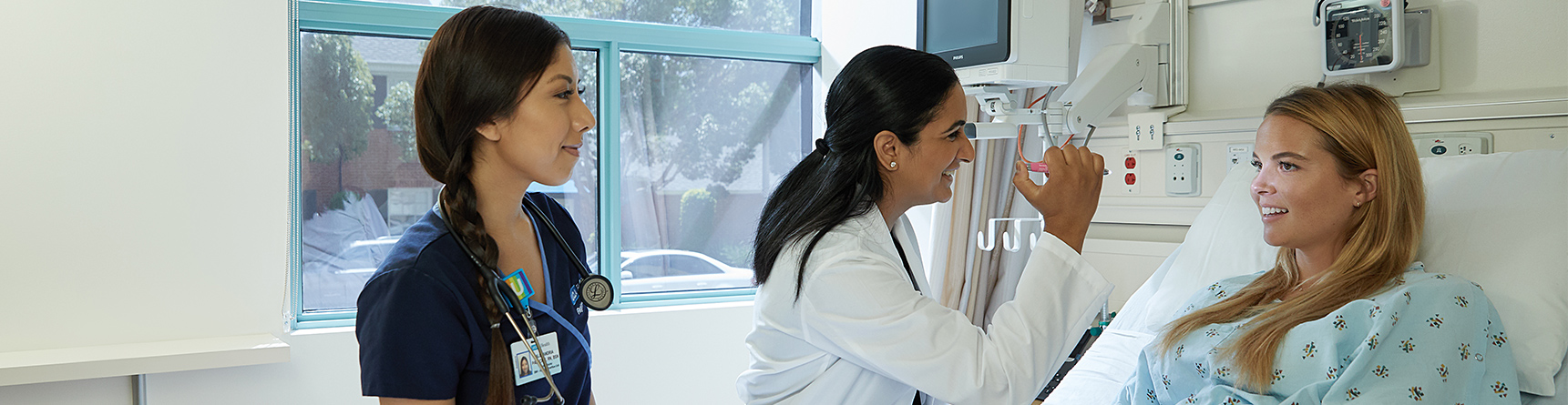 Female physician and female nurse examining female patient at hospital bedside