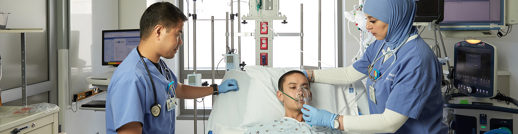Female respiratory therapist placing oxygen mask on male patient in hospital bed while male nurse looks on