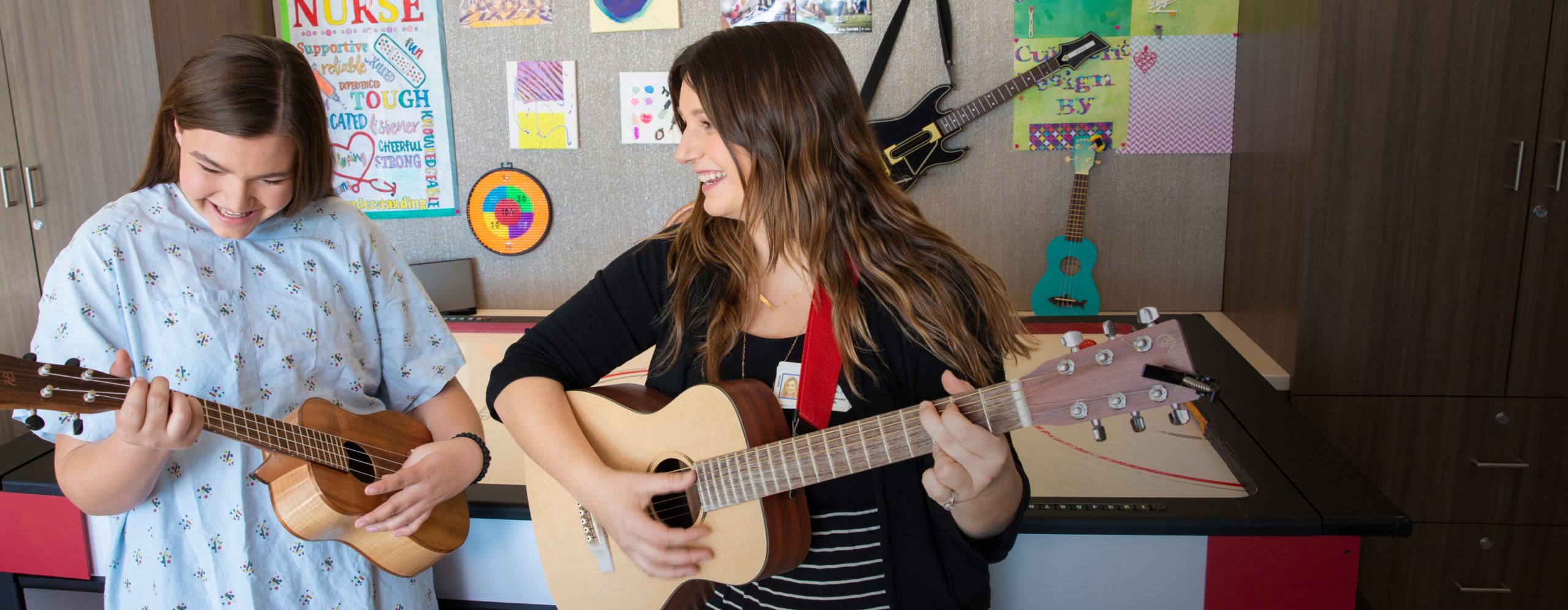 A smiling UCLA Health music therapist playing guitar with a smiling patient playing the ukulele
