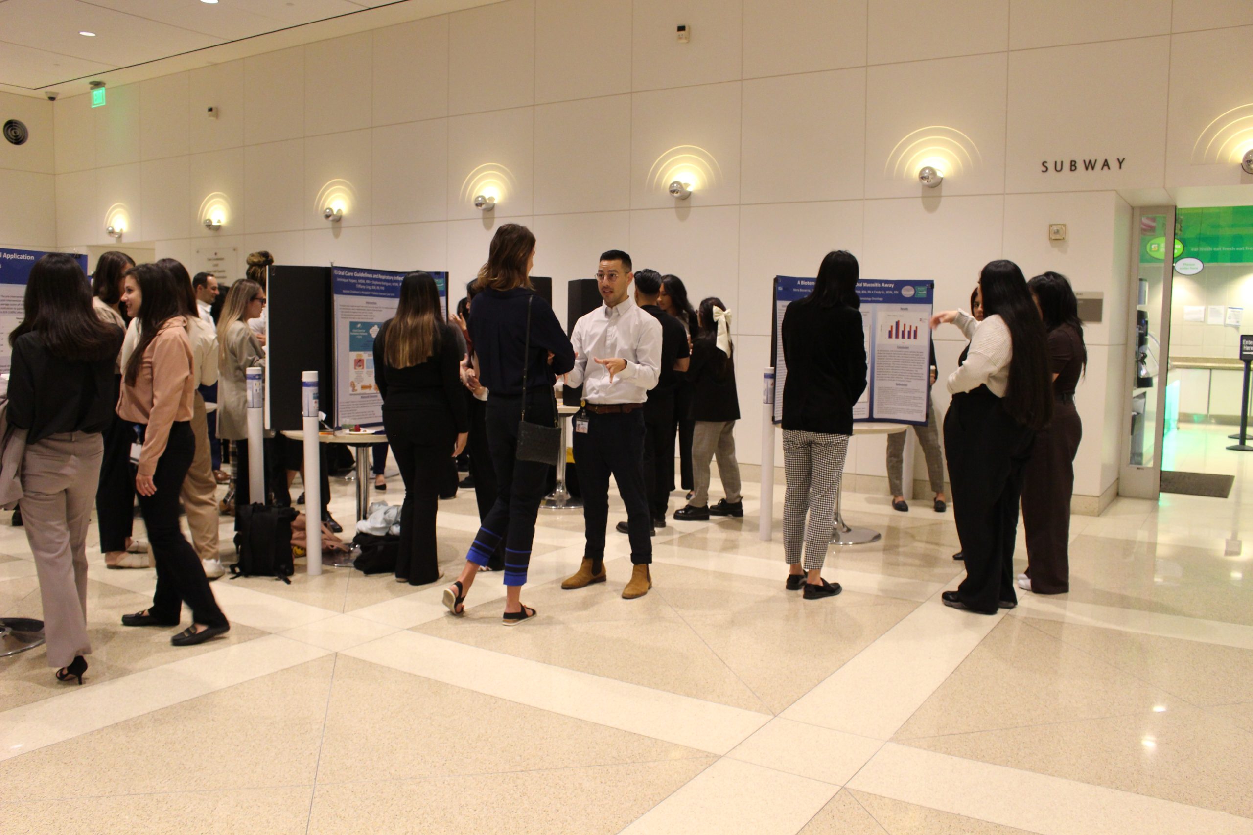 People in business attire engage in discussions and view research posters at an indoor event.