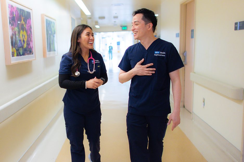 A smiling patient in a hospital bed with a nurse in blue scrubs caring for him, surrounded by medical equipment.