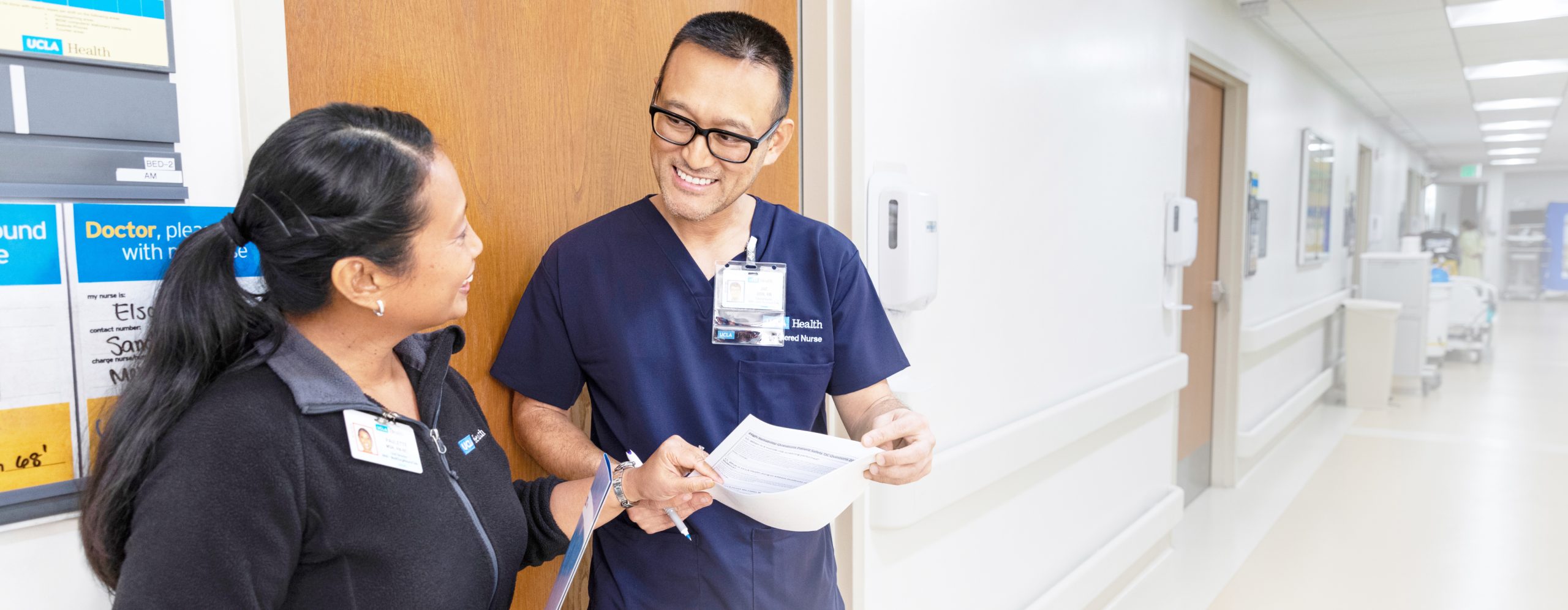 A male and a female UCLA Health nurse speaking with each other in a hospital hallway