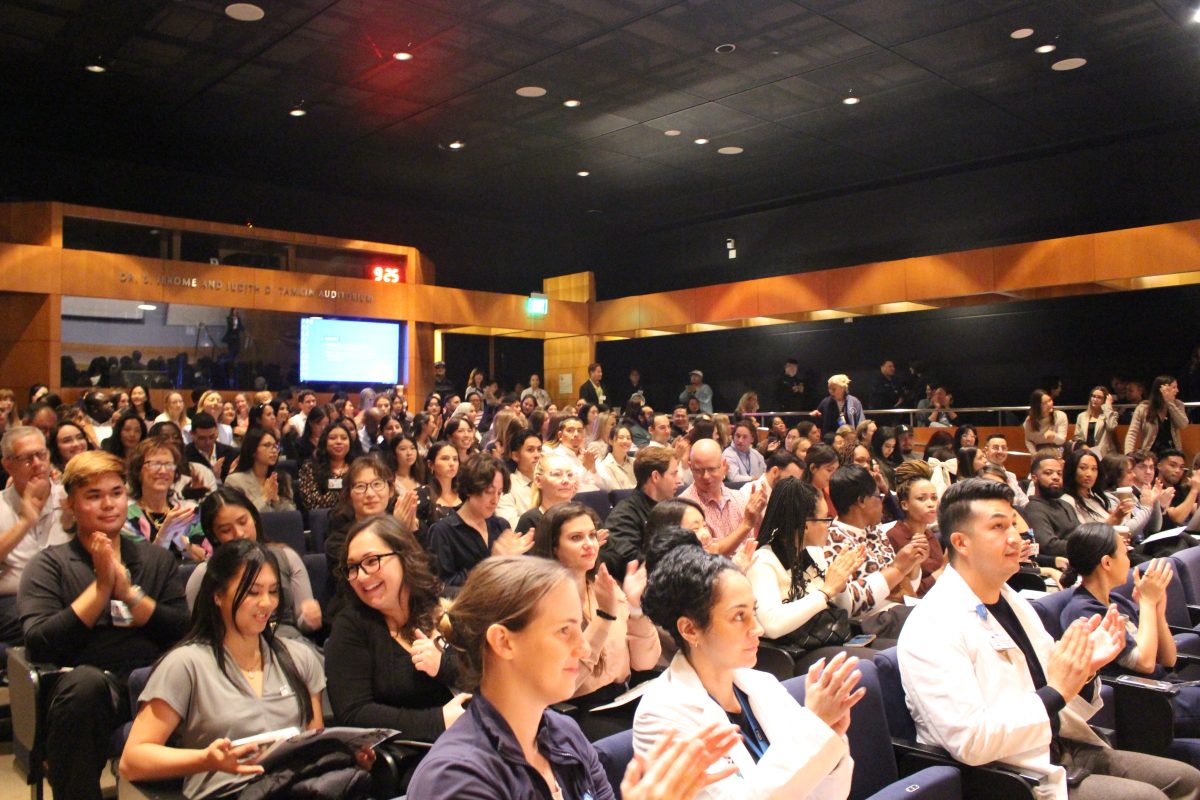 A large audience seated in an auditorium applauds.