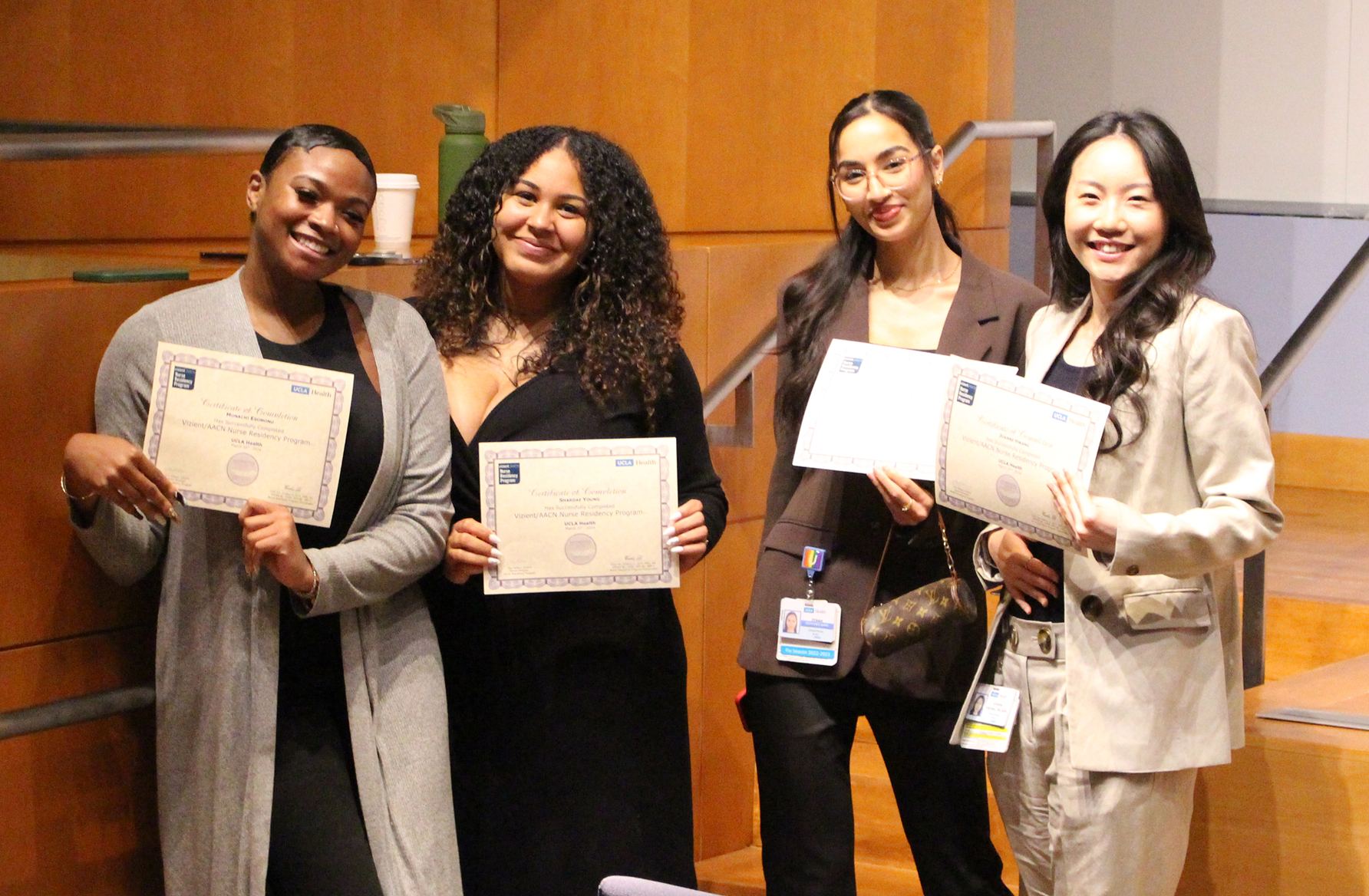 Four smiling women in different ethnicities pose with certificates at a facility.